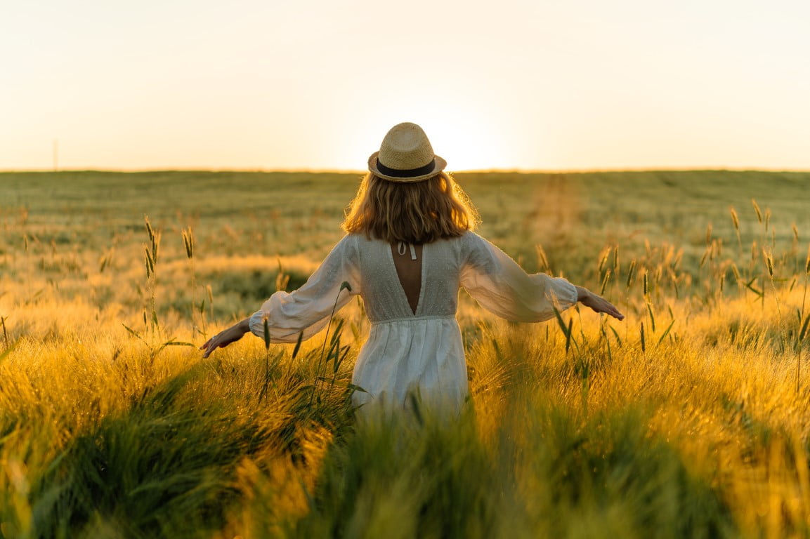 Femme avec un chapeau de paille qui marche dans un champs de blé au soleil