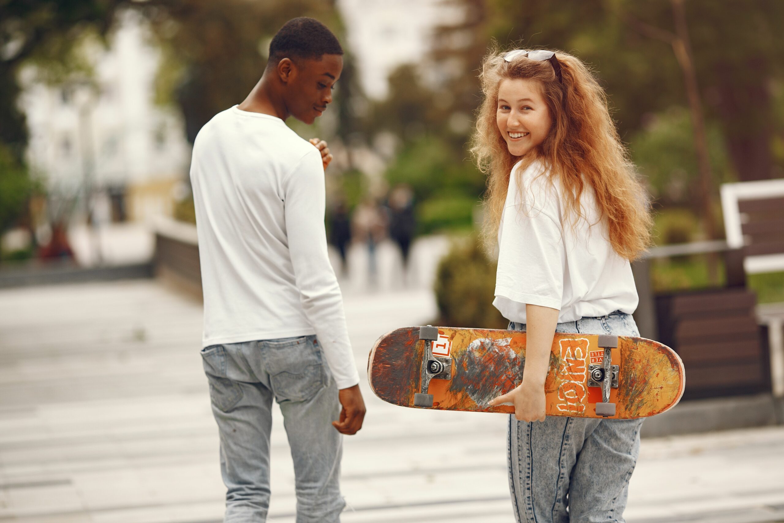 Un couple interracial heureux faisant du skateboard dans le parc, profitant d'une belle journée ensoleillée ensemble.