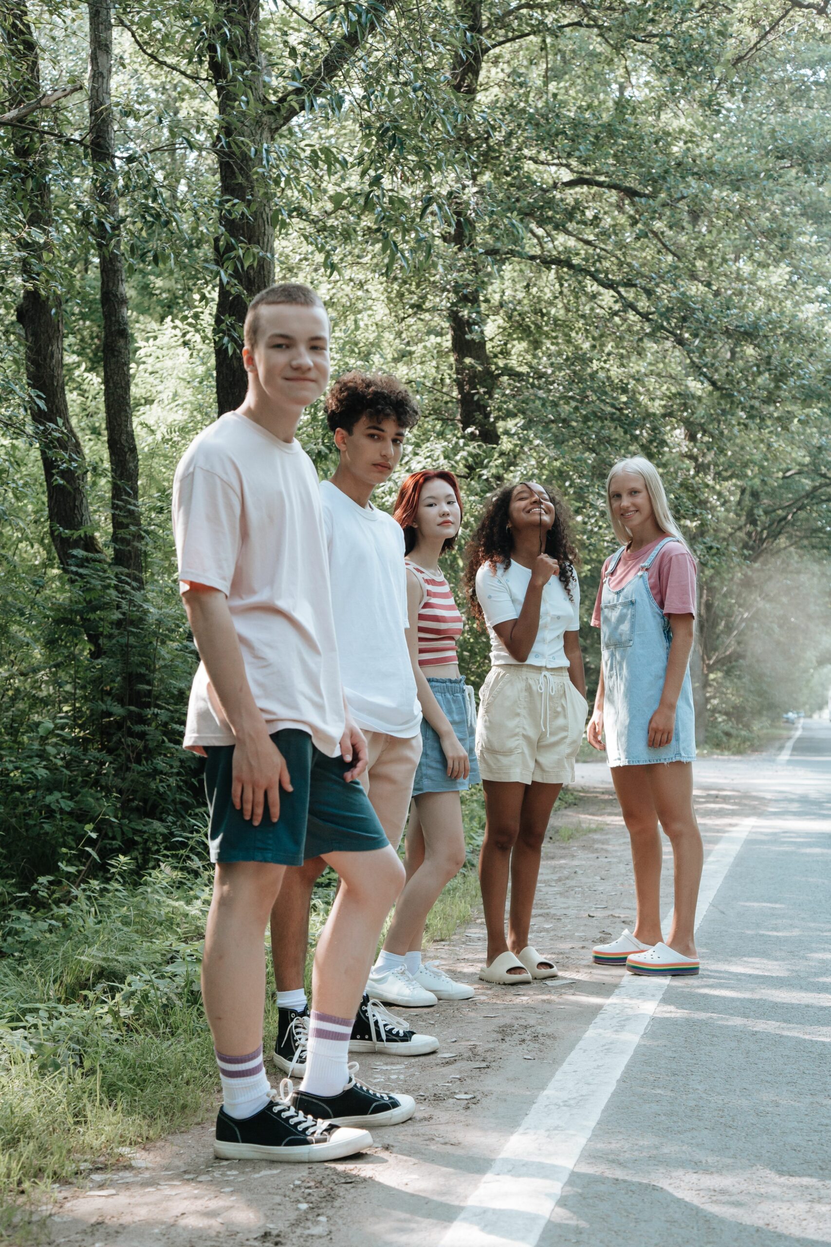 Groupe diversifié d'adolescents se relaxant près d'une route forestière, profitant d'une journée d'été ensoleillée.
